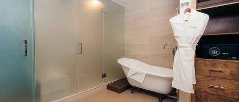 Un baño moderno con ducha envuelta en vidrio, una bañera independiente y un tocador de madera con un dispositivo electrónico negro.