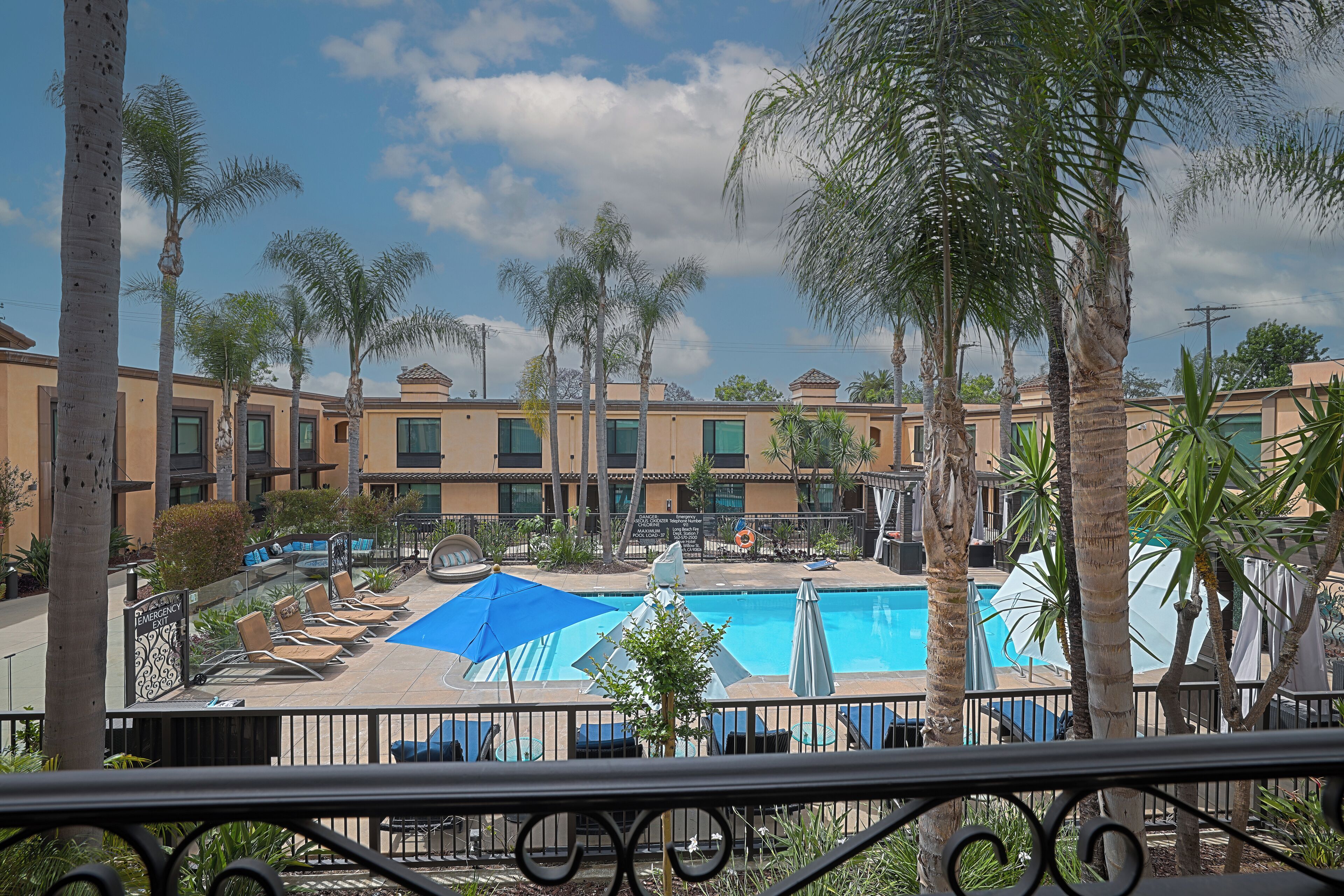 A pool area with lounge chairs and umbrellas, surrounded by palm trees and a building with multiple windows.
