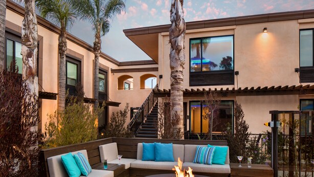 A modern outdoor living area with a fire pit, seating, and palm trees. - The Cove Hotel, Long Beach (Long Beach)