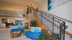 A spacious lobby with a curved blue sofa, a wooden coffee table, and a staircase with a black railing. - The Cove Hotel, Long Beach (Long Beach)