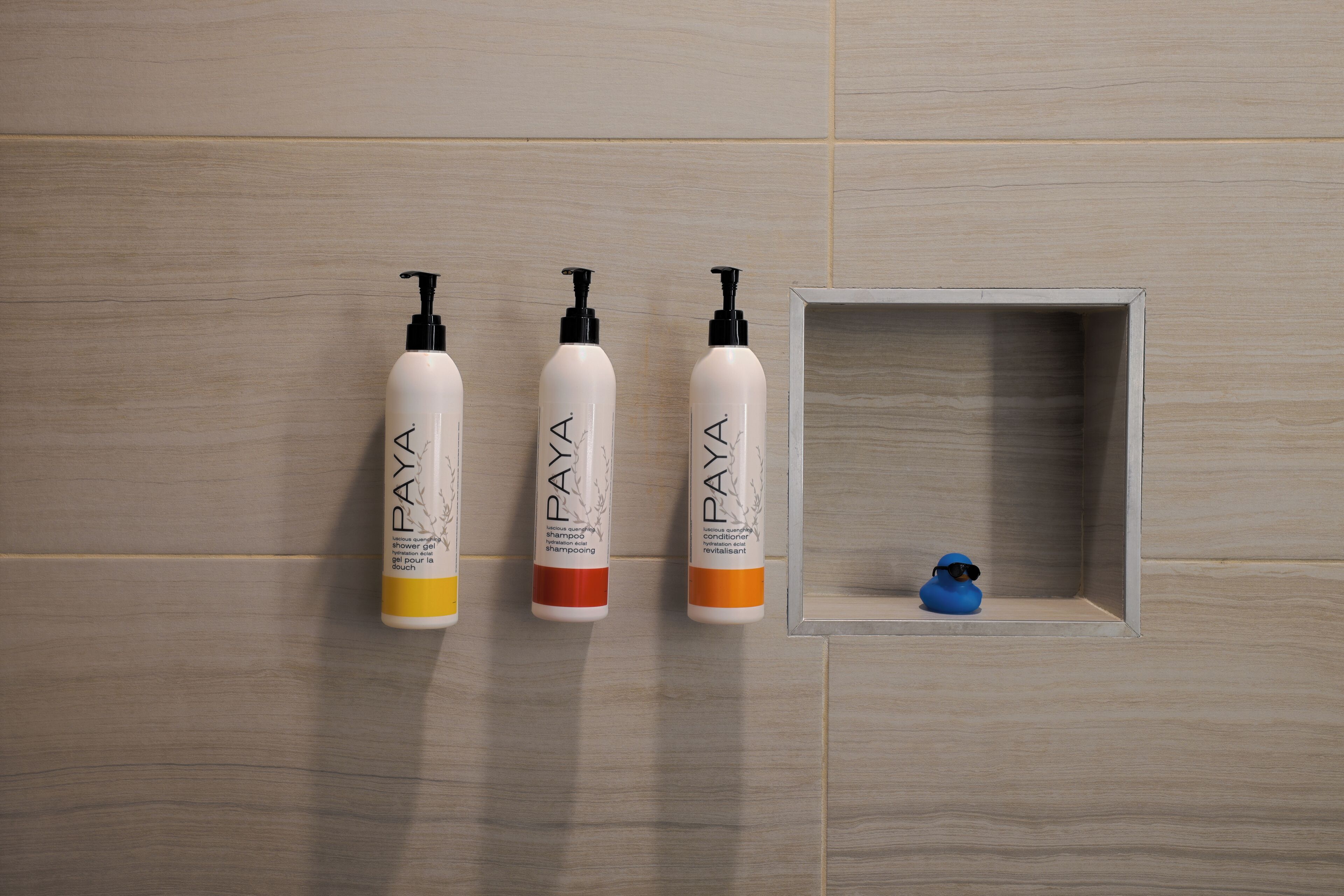 Drie flessen shampoo en conditioner, een klein blauw eendje en een houten wand.