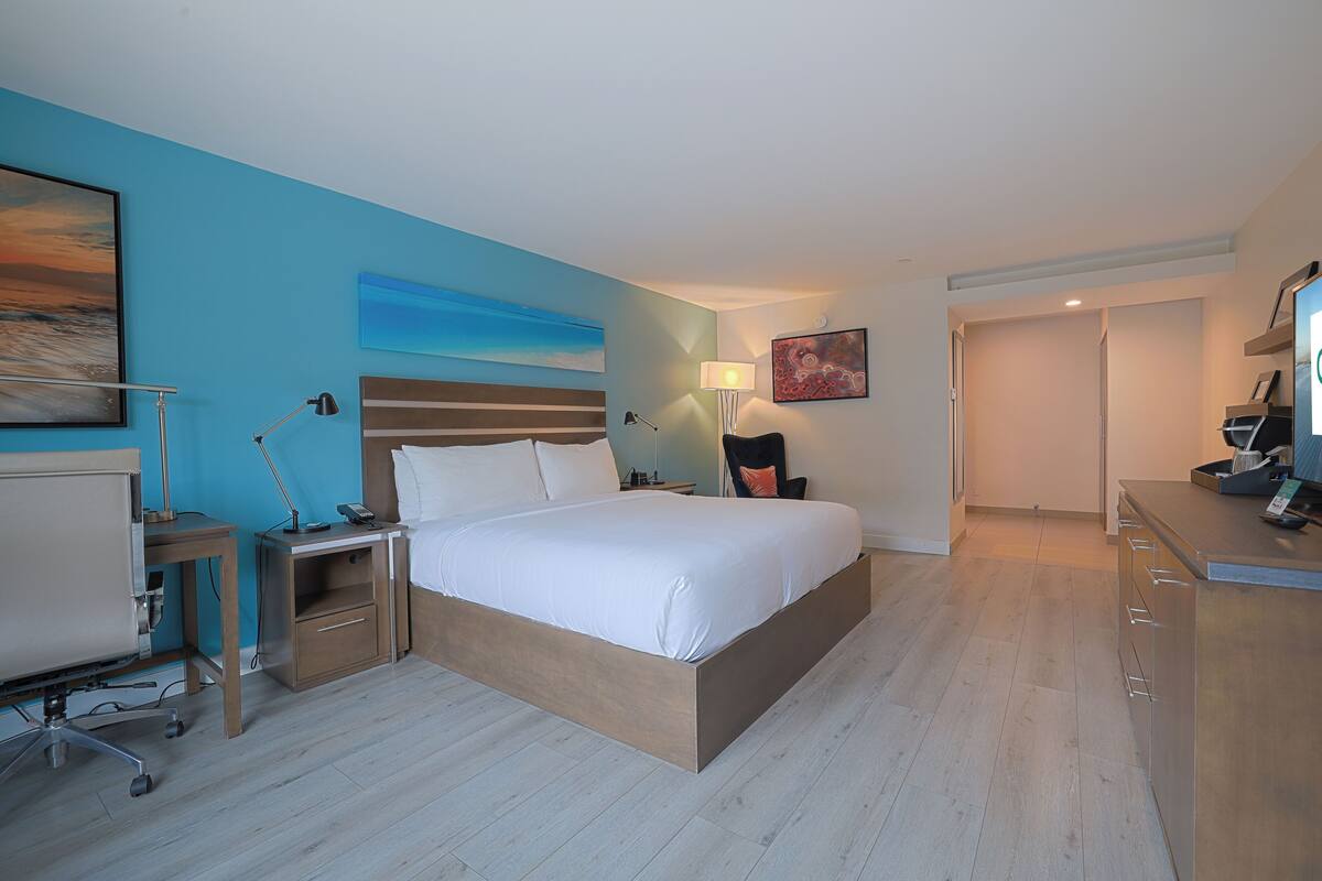 A modern hotel room with a large bed, bedside tables, a desk, and a chair.