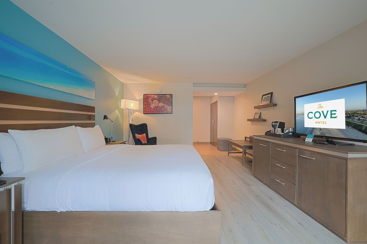 A hotel room with a large bed, a desk, a chair, a TV, and a painting on the wall.