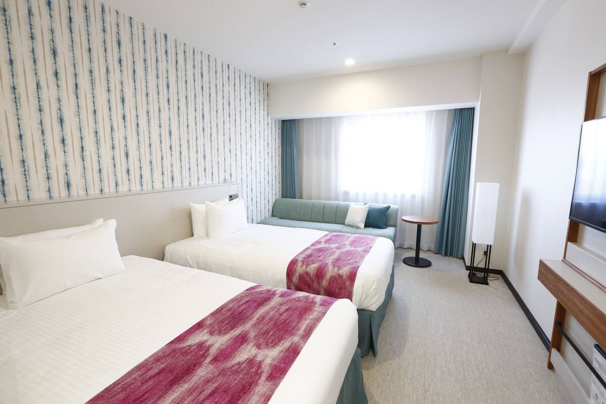 Habitación de hotel con dos camas, un sofá, un televisor y una mesita.