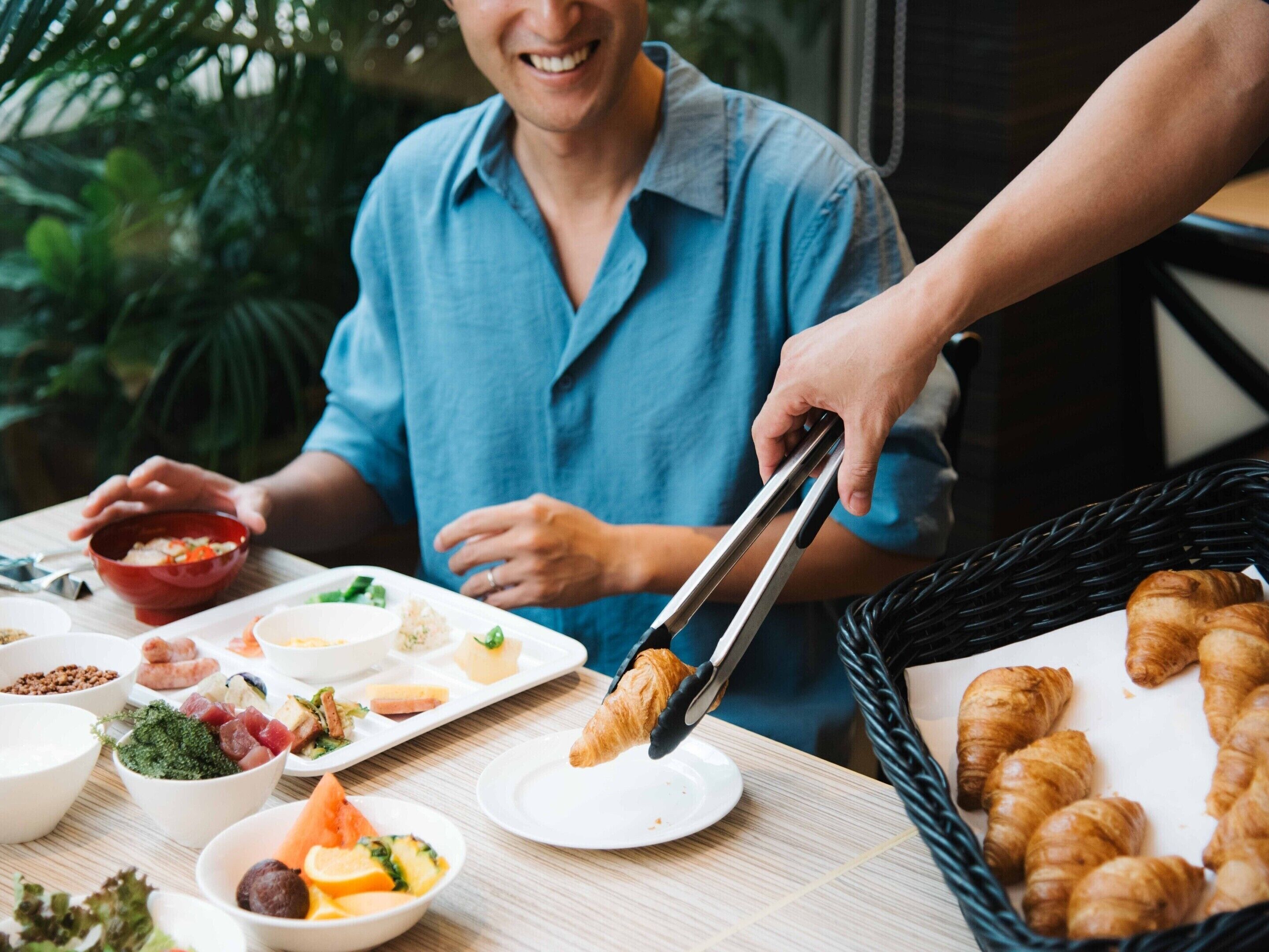 A dining table with various food items and a basket of croissants.