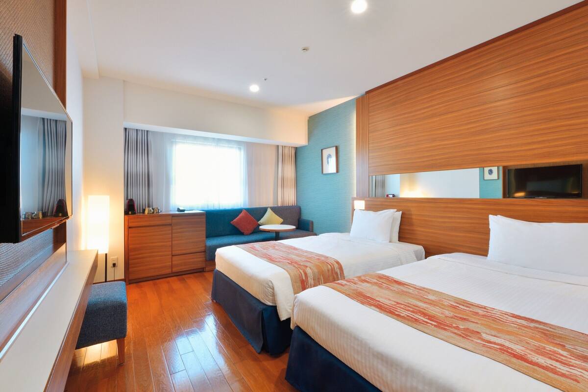Una habitación de hotel con dos camas, un sofá, un televisor y una ventana con cortinas.