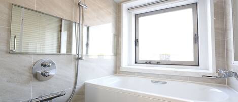 Un baño moderno con una bañera grande, ducha, inodoro y ventana que proporciona luz natural.