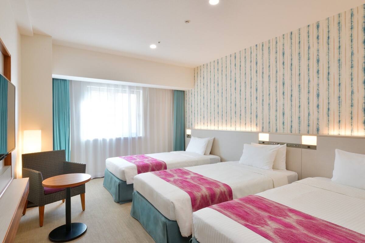 Habitación de hotel con dos camas, un escritorio, una silla y un televisor.