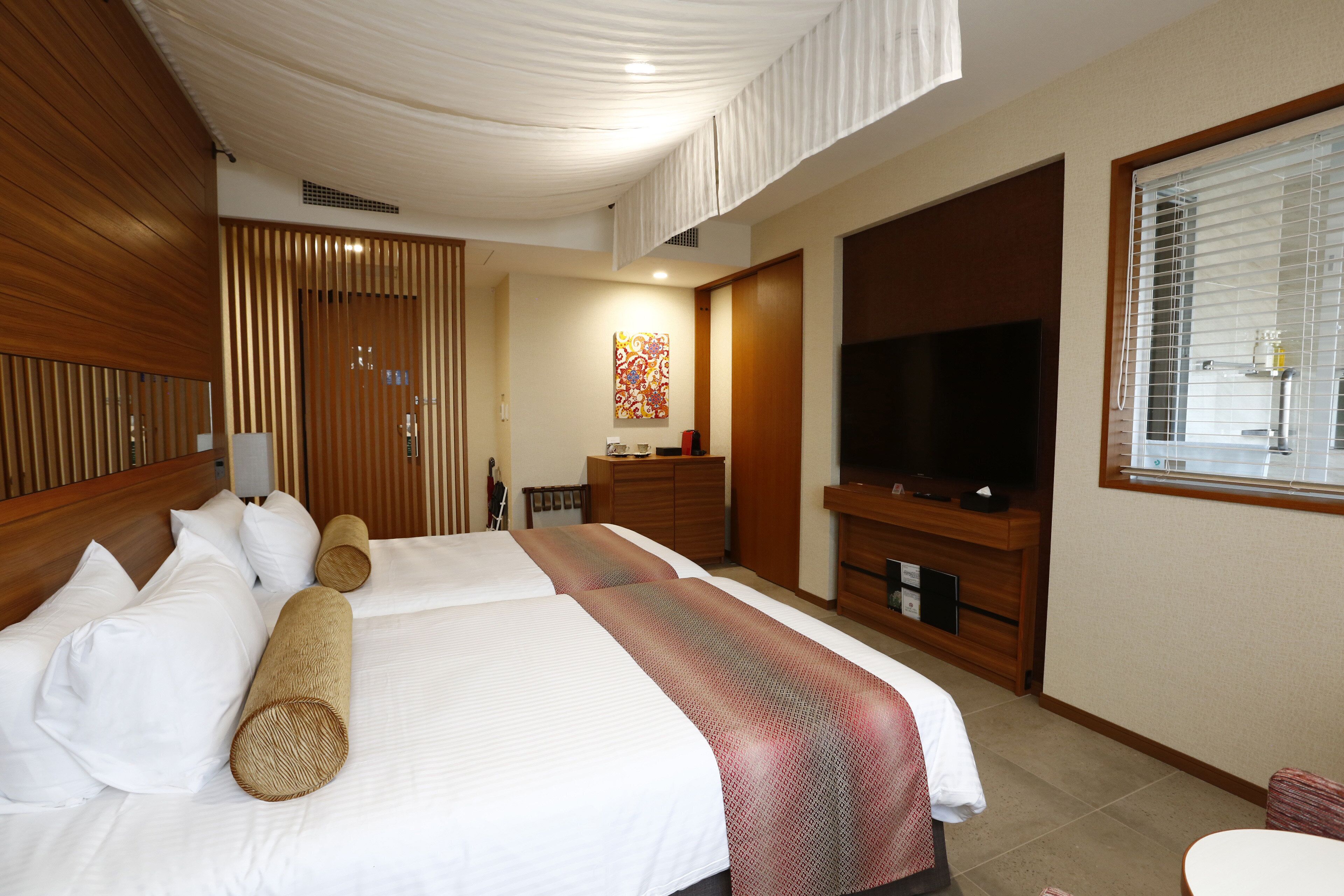 Une chambre d’hôtel avec un grand lit, une télévision, une armoire en bois et une fenêtre avec des stores.