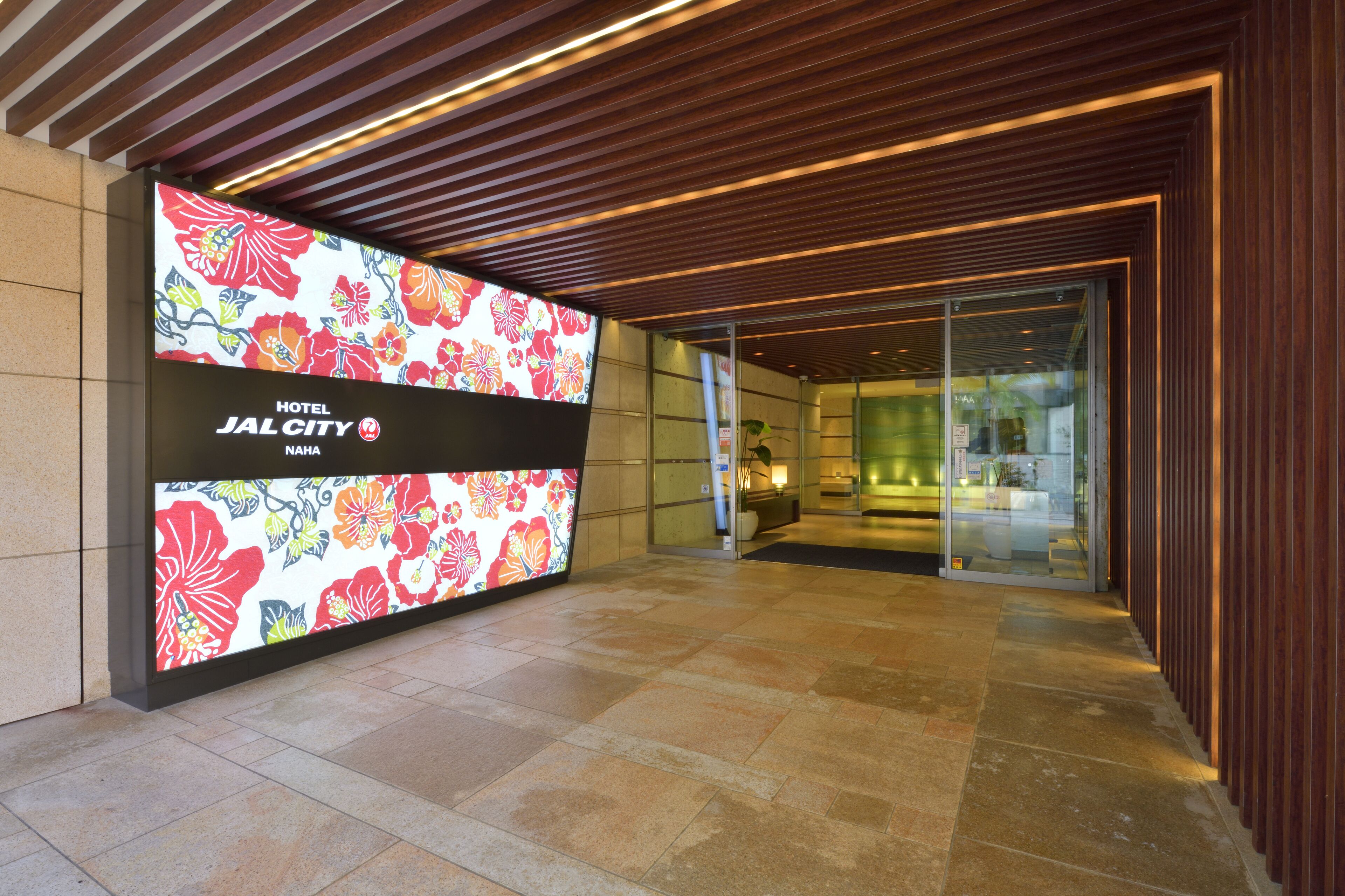 Una entrada de hotel moderna con un gran panel digital floral, una zona de recepción y una puerta de cristal que da al interior.