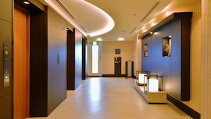 Un pasillo moderno de hotel con un ascensor de madera, un mostrador de recepción y una pared con paneles decorativos.