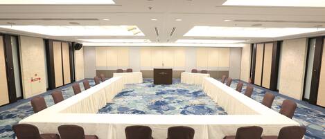 A conference room with a long table and chairs, a podium, and a carpeted floor.