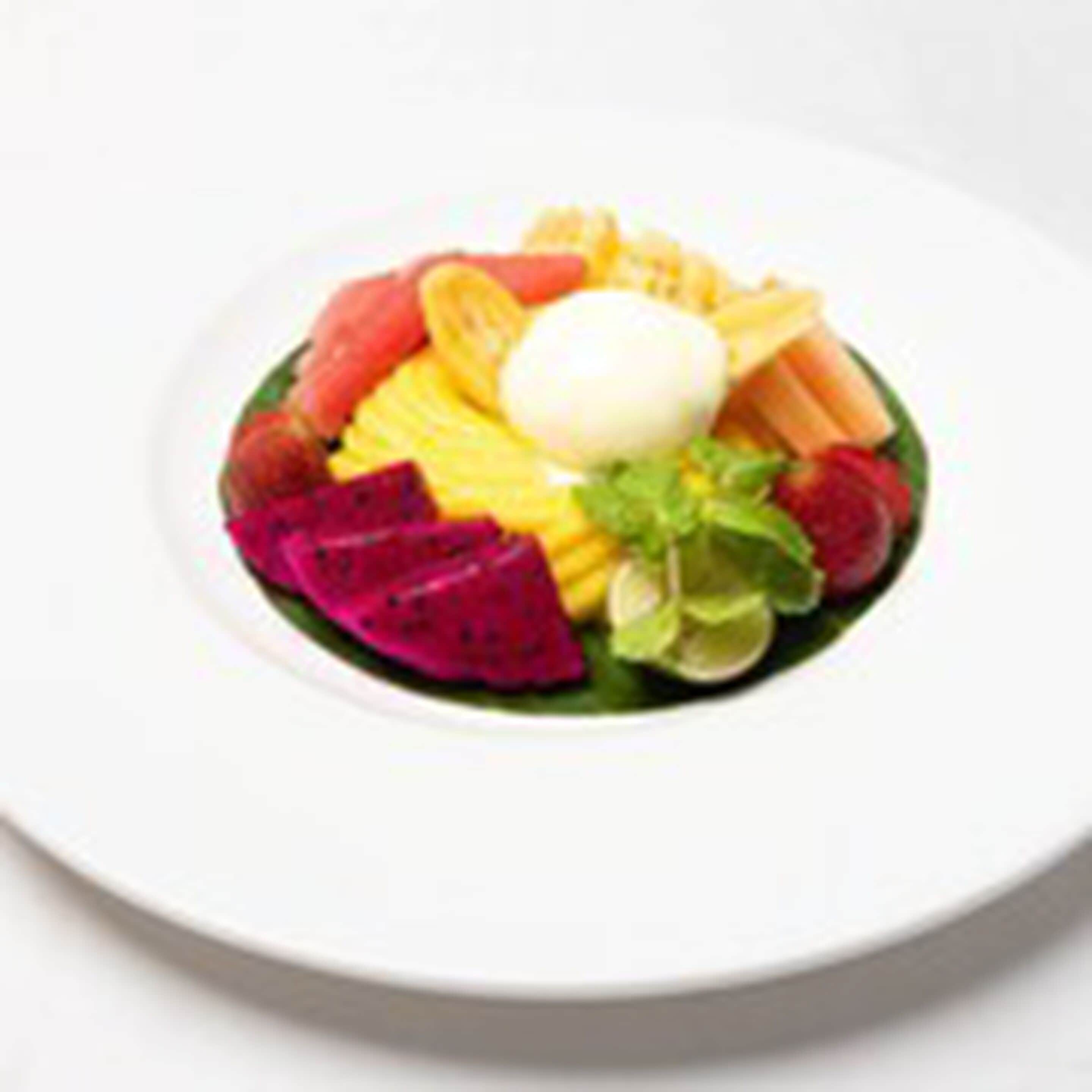 A white plate with a variety of fruits and a white sphere, possibly a dessert, arranged on a green leaf.