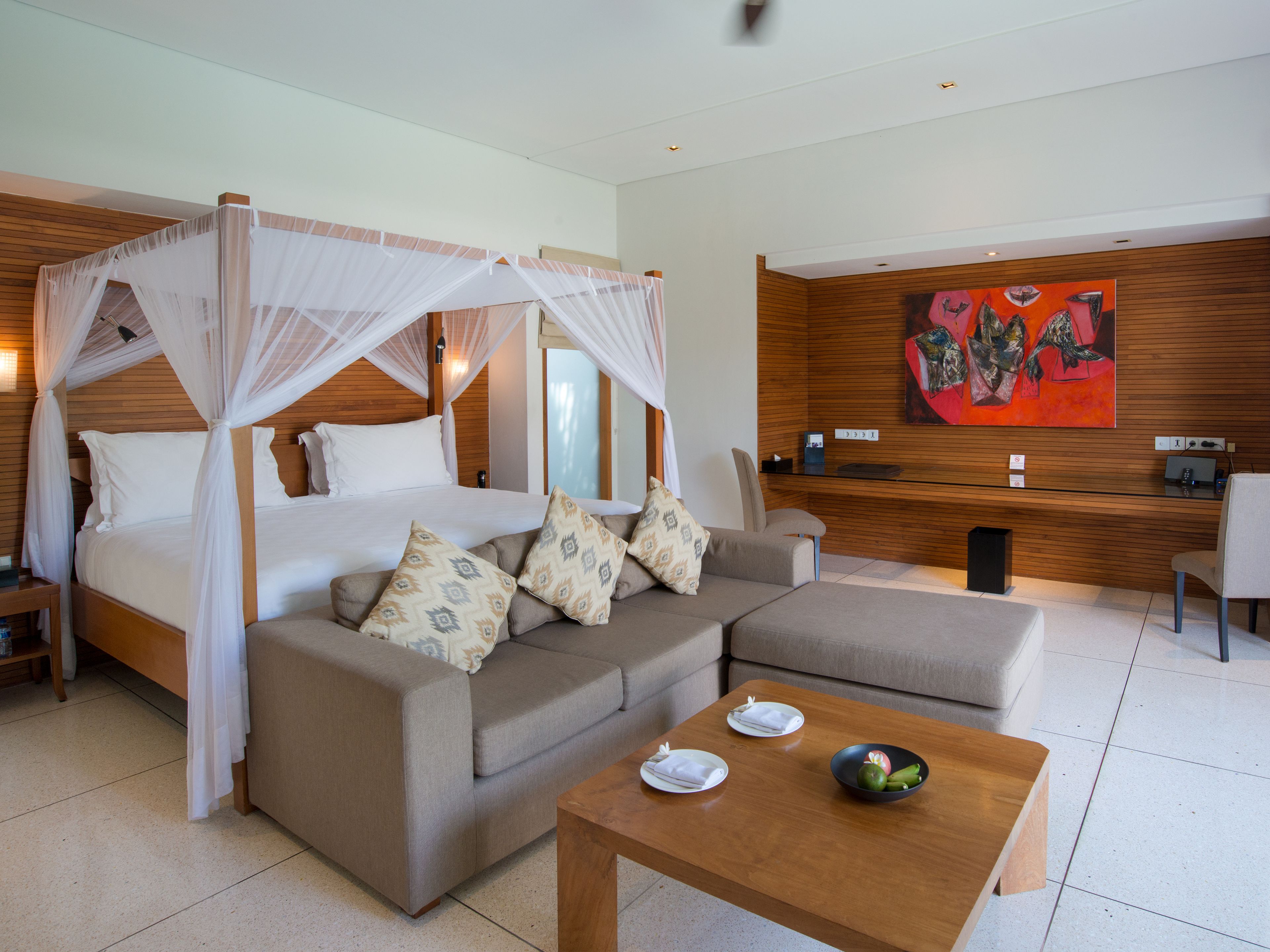 A modern hotel room with a bed, a sofa, a coffee table, and a desk area.