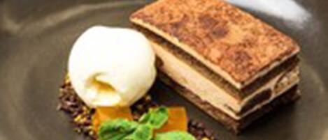 Un postre con una tarta en capas y una bola de helado sobre un plato oscuro.