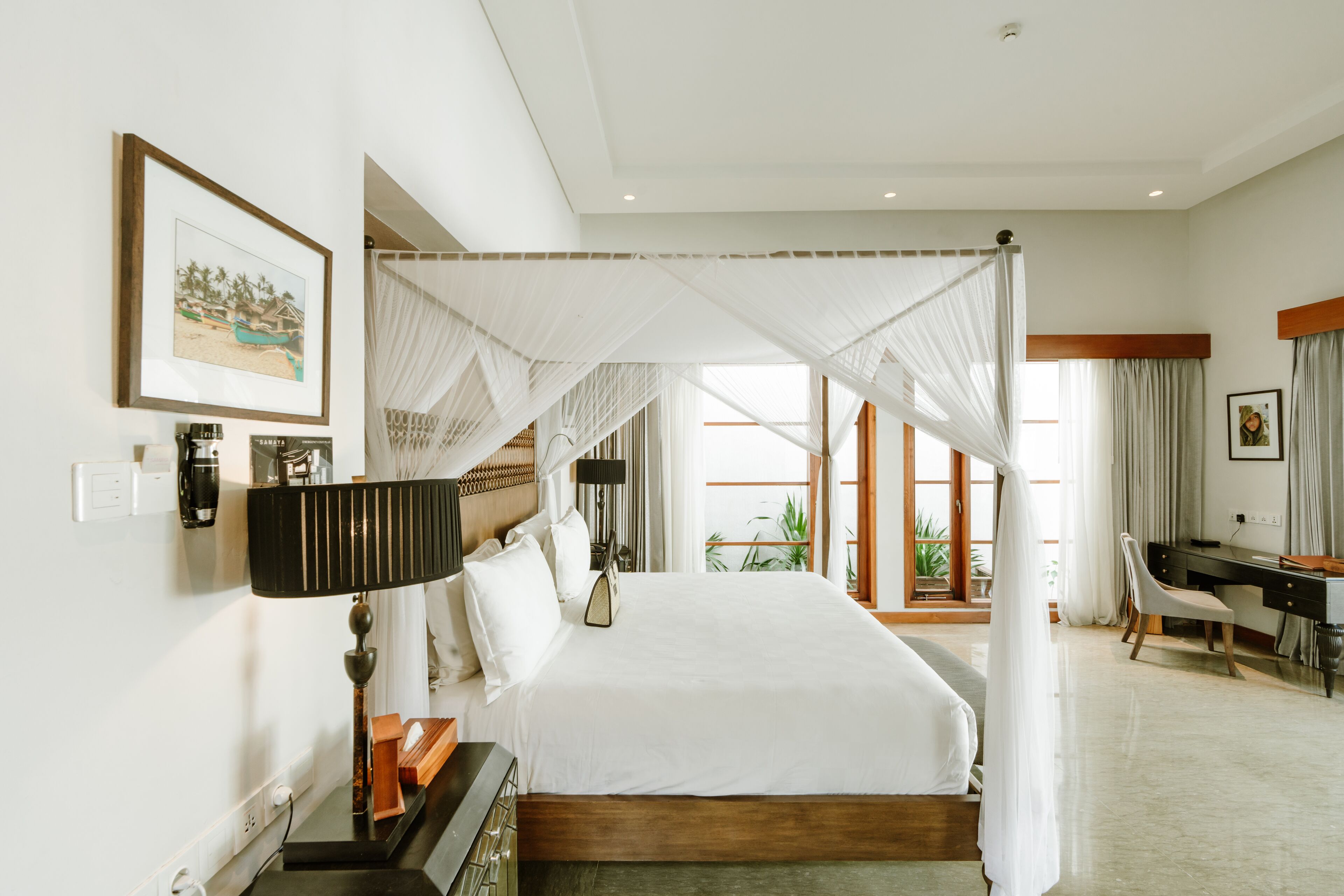A spacious bedroom with a large bed, a desk, and a chair, featuring a canopy bed and a view of the outdoors.