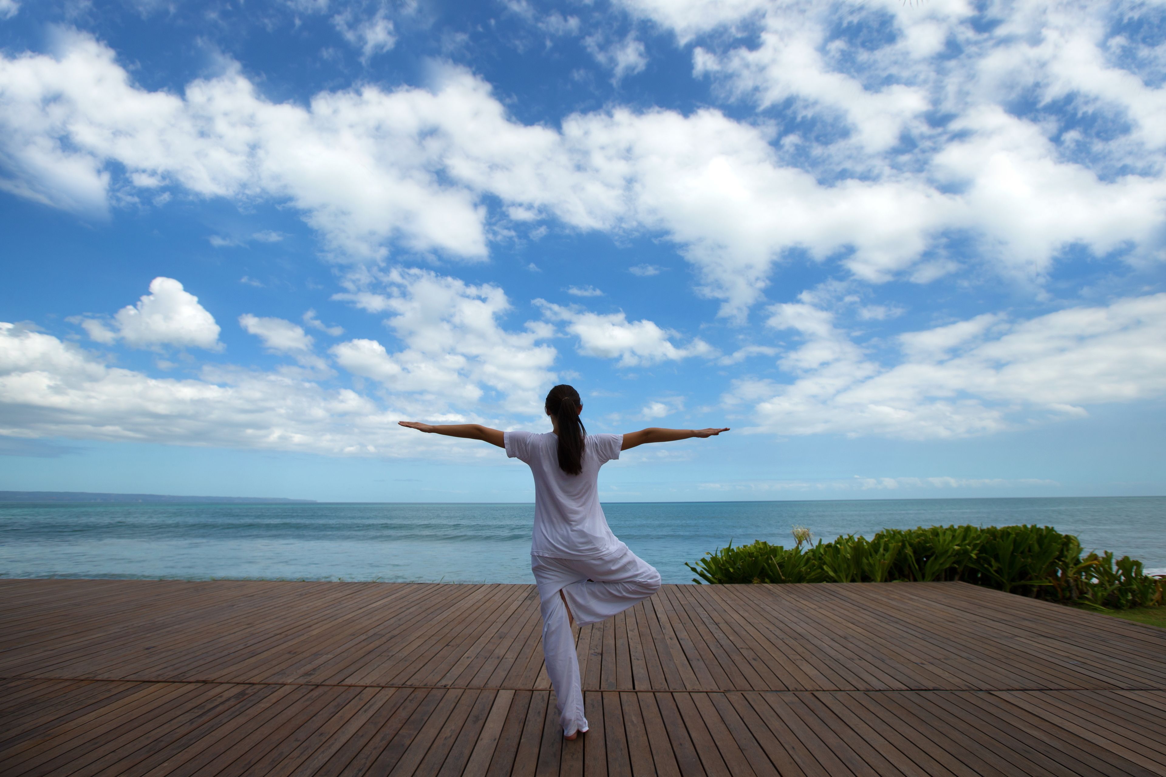 Una persona esegue una posa yoga su un molo di legno con vista sull'oceano e sul cielo.