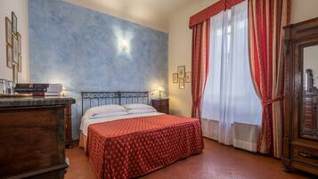 Un dormitorio con cama, cómoda, mesita de noche, lámpara de pared y ventana con cortinas.