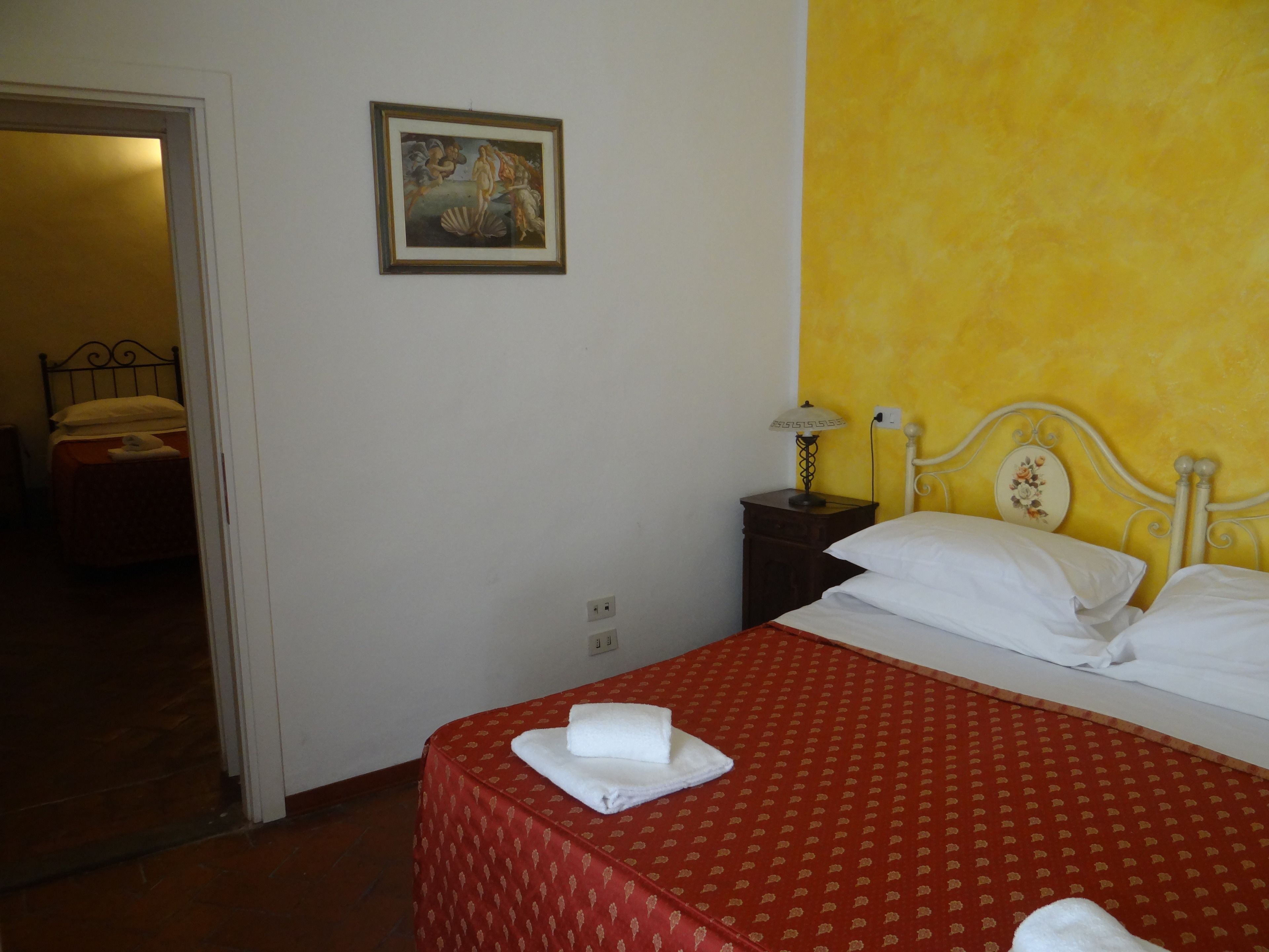 Una habitación de hotel con una cama, una mesita de noche, una lámpara y un cuadro en la pared.