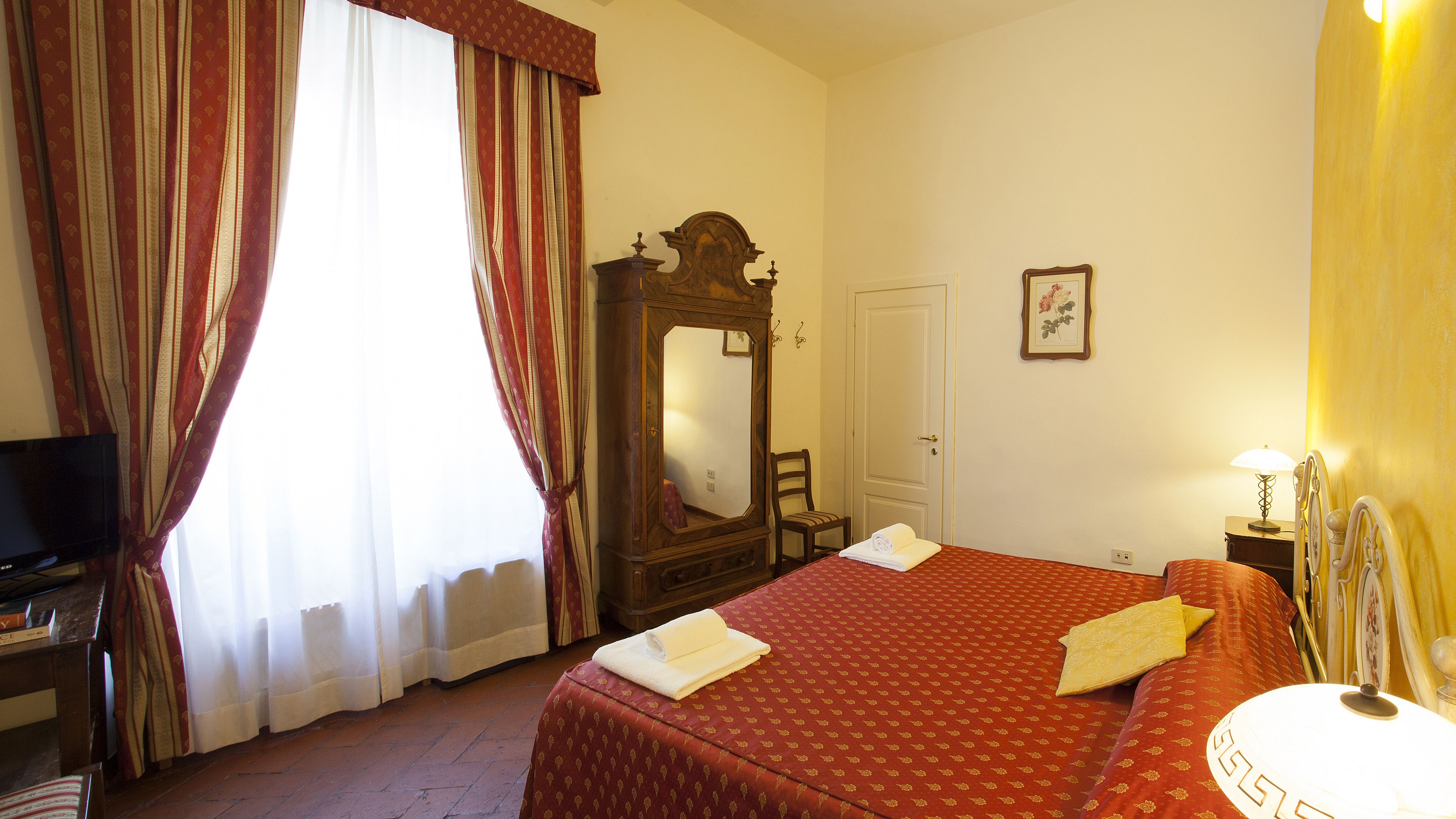 Une chambre d’hôtel avec un grand lit, une commode en bois, une télévision et un miroir.