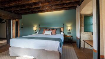 Une chambre avec un grand lit, des poutres en bois, un mur en pierre et une porte verte.