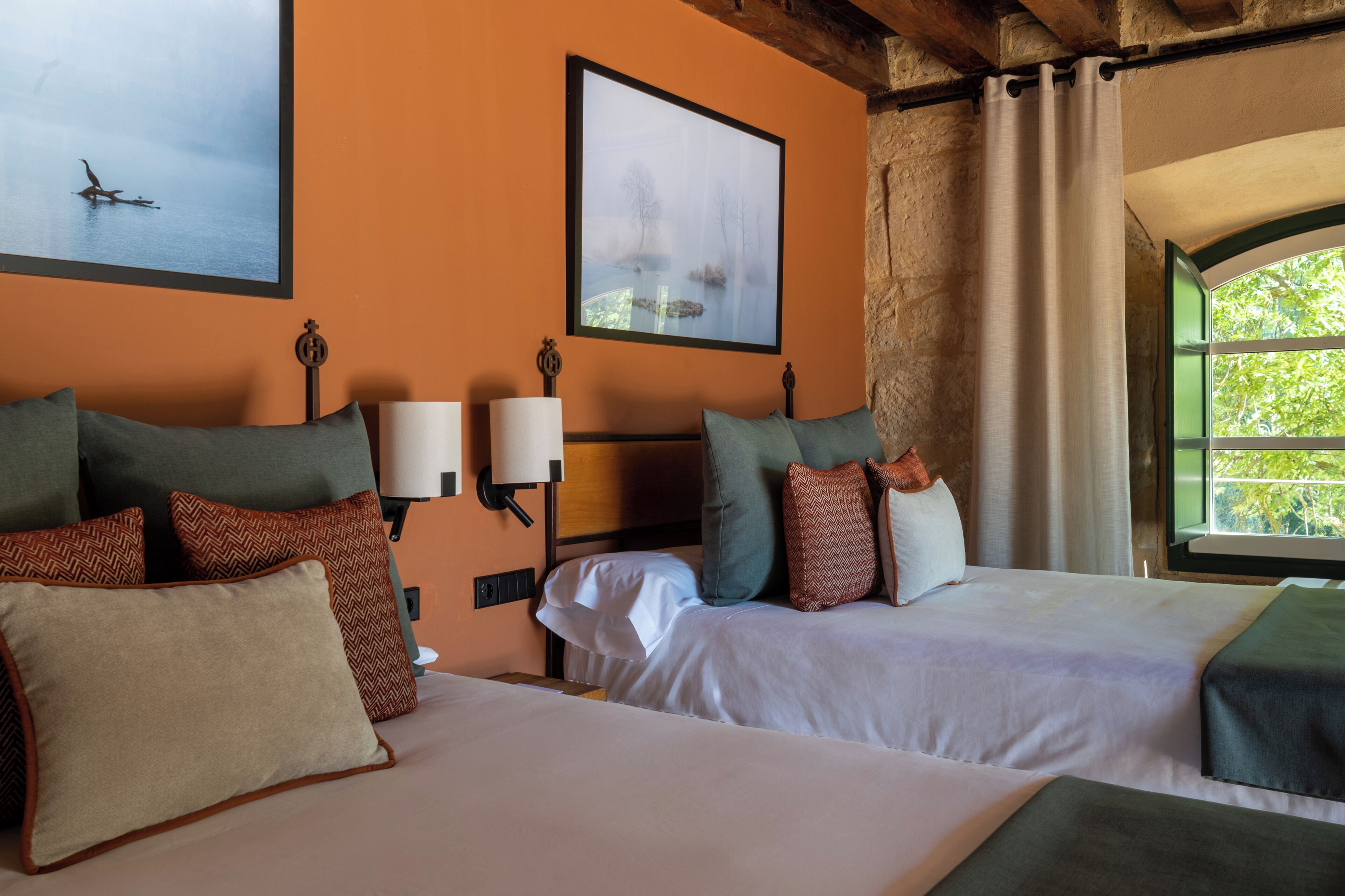 A hotel room with two beds, a nightstand, a lamp, a framed picture, and a window with a view.