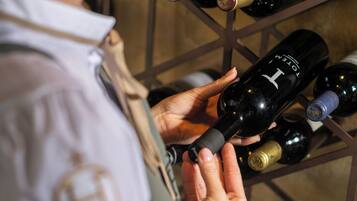Une personne tenant une bouteille de vin, avec une étagère remplie de bouteilles de vin en arrière-plan.