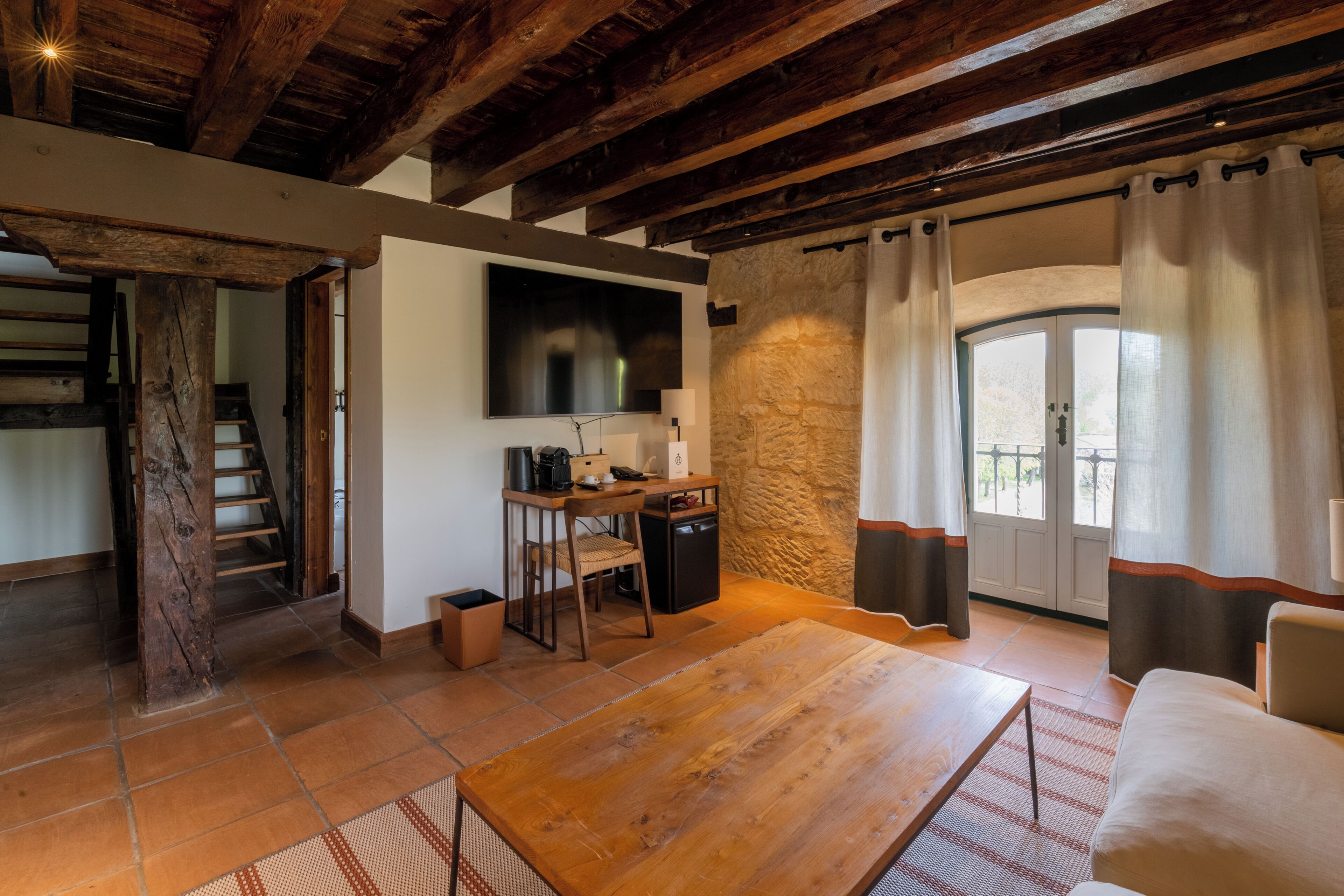 Una habitación rústica con una mesa de madera, un sofá, un televisor y una pared de piedra.