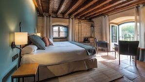 A bedroom with a bed, bedside table, lamp, chair, and a view of the outdoors.