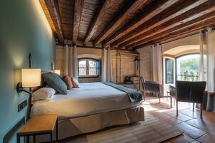 Un dormitorio con cama, mesita de noche, lámpara, silla y vistas al exterior.
