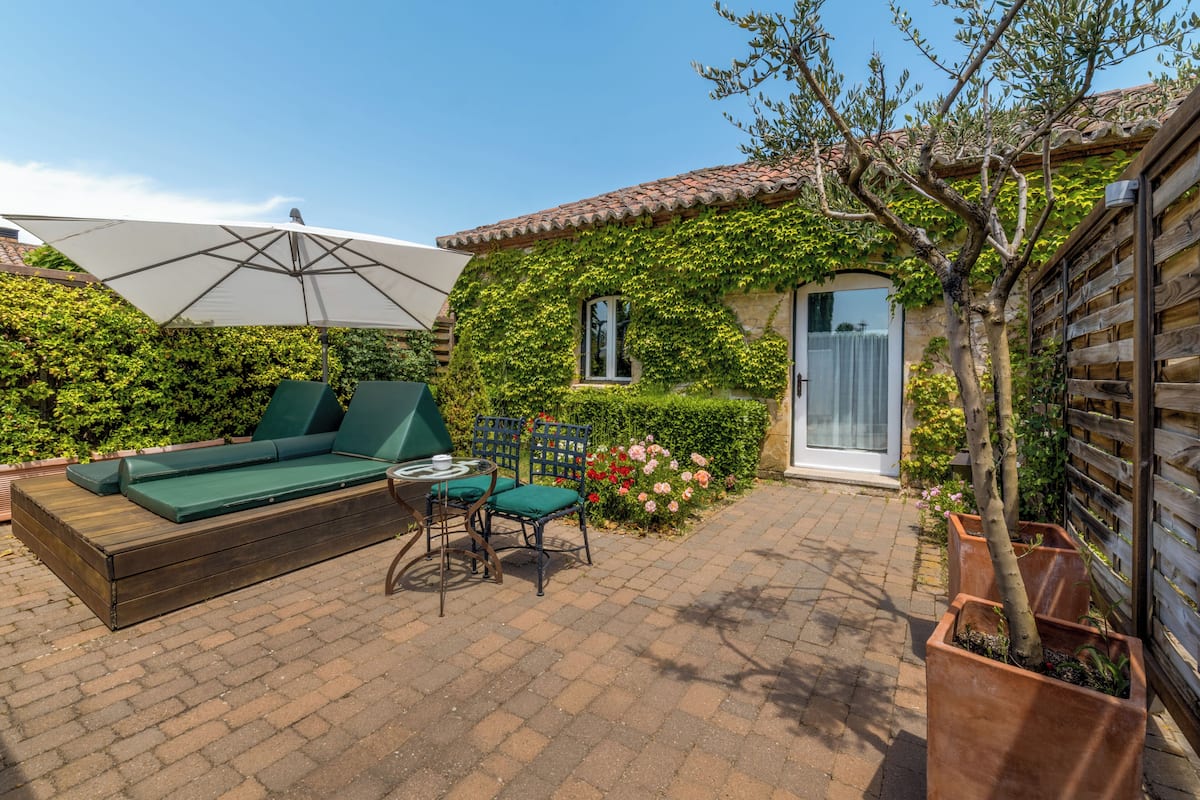 Une terrasse avec un banc en bois, des chaises et un grand parasol.
