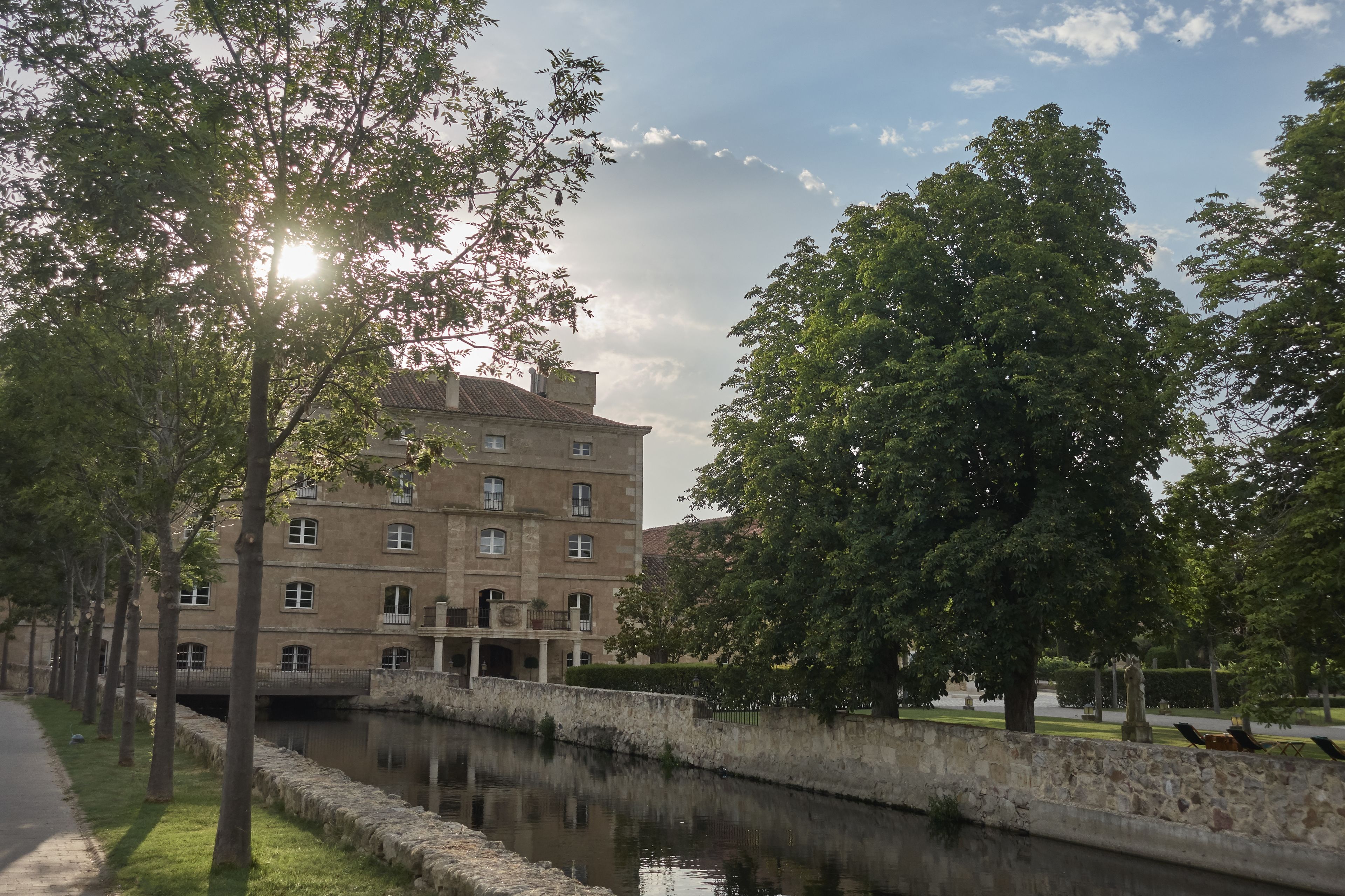 A historic building with multiple windows and a stone wall beside a calm waterway.
