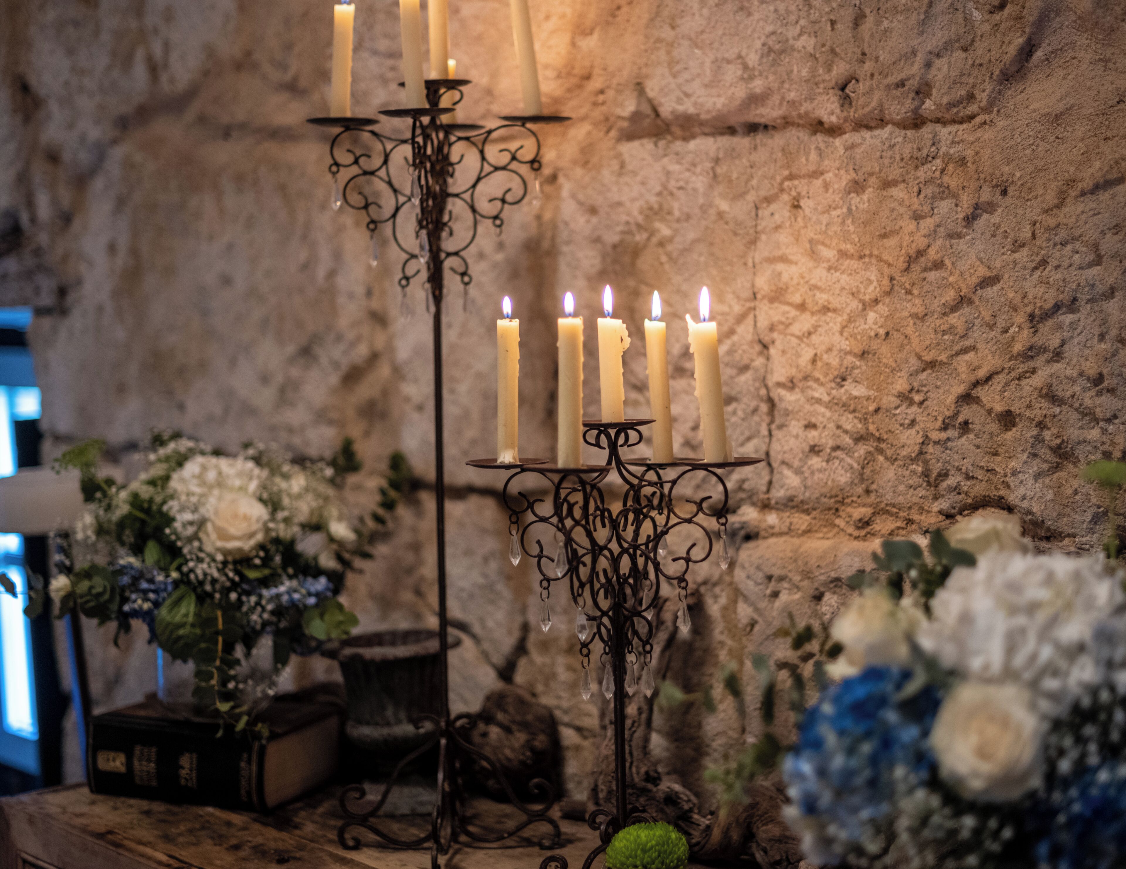 Un candelabro con múltiples velas, una pared de piedra rústica y arreglos florales.