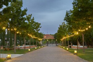 Un camino conduce a un edificio de techo rojo, bordeado por árboles y luces colgantes.