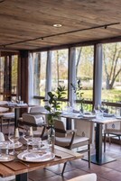 Un restaurante con mesas dispuestas para comer, ventanas amplias y vistas al exterior.