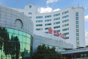 A modern building with a curved glass facade and a large sign on the side. - Media Center Hotel (Beijing)