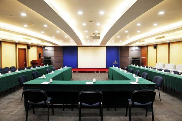 Uma sala de conferências com uma mesa comprida, cadeiras, uma tela de projetor e um palco.