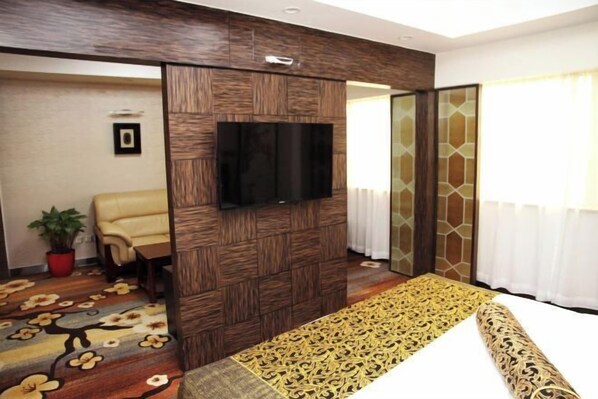A hotel room with a bed, a TV mounted on a wooden panel, a chair, and a potted plant.