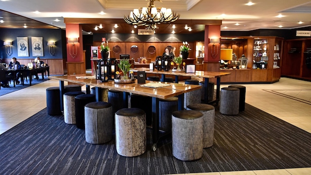 Eine Hotelhalle mit Empfangsbereich, einem Kronleuchter und einer Sitzecke mit runden Hockern.