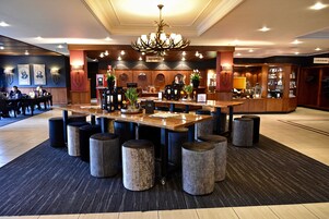 Vestíbulo de hotel con mostrador de recepción, un candelabro y una zona de estar con taburetes redondos.