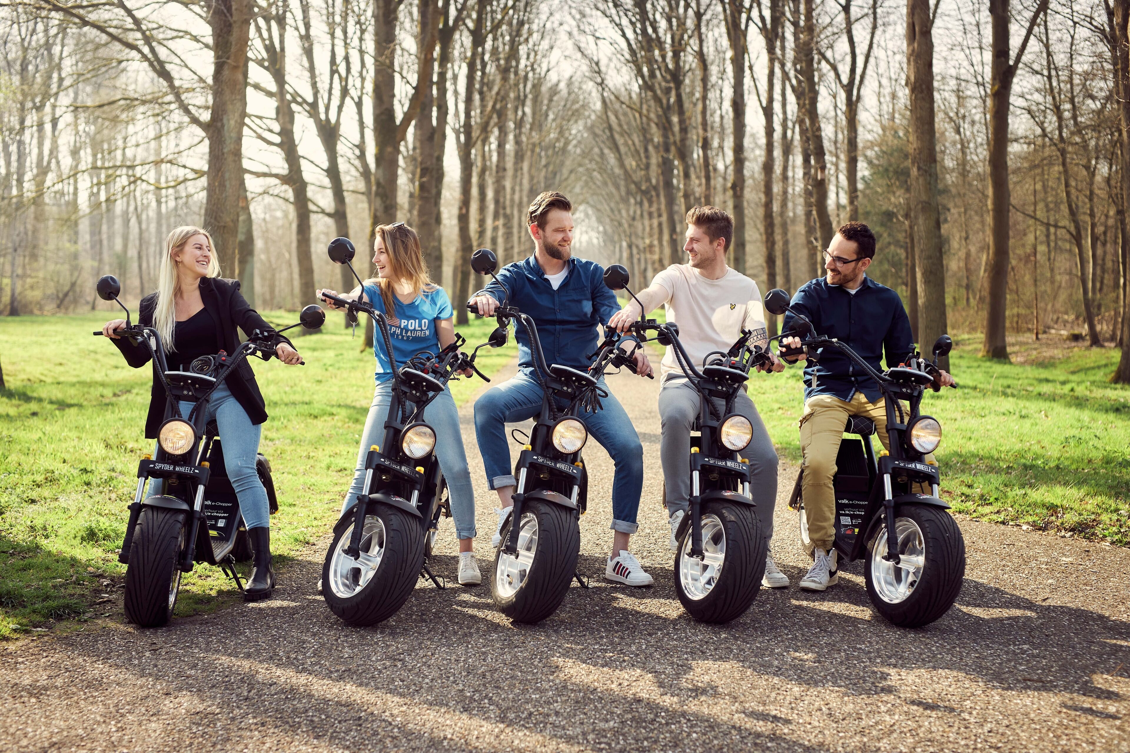 Four people riding electric scooters on a path in a park.