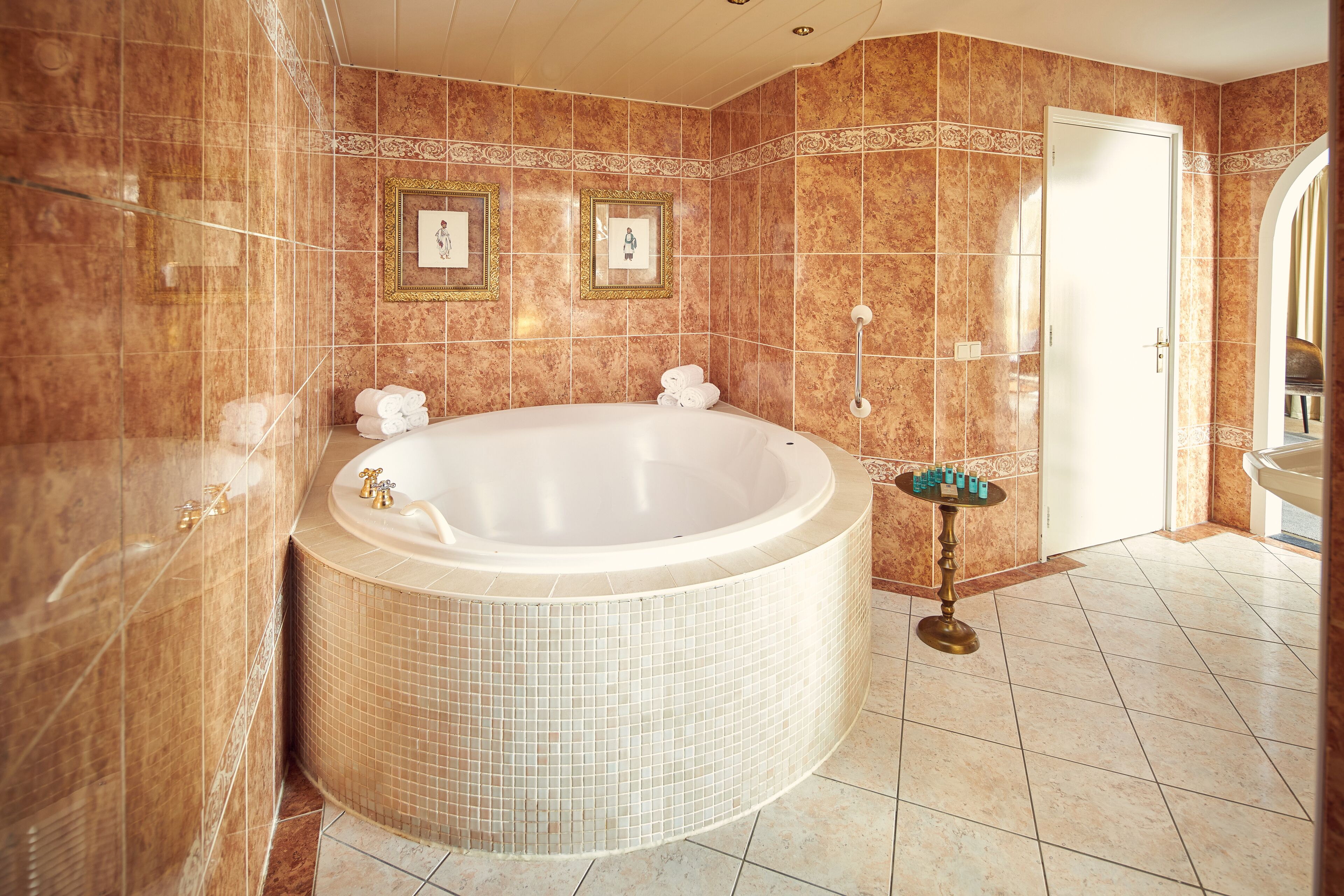 A large, round bathtub in a bathroom with tiled walls and a door.