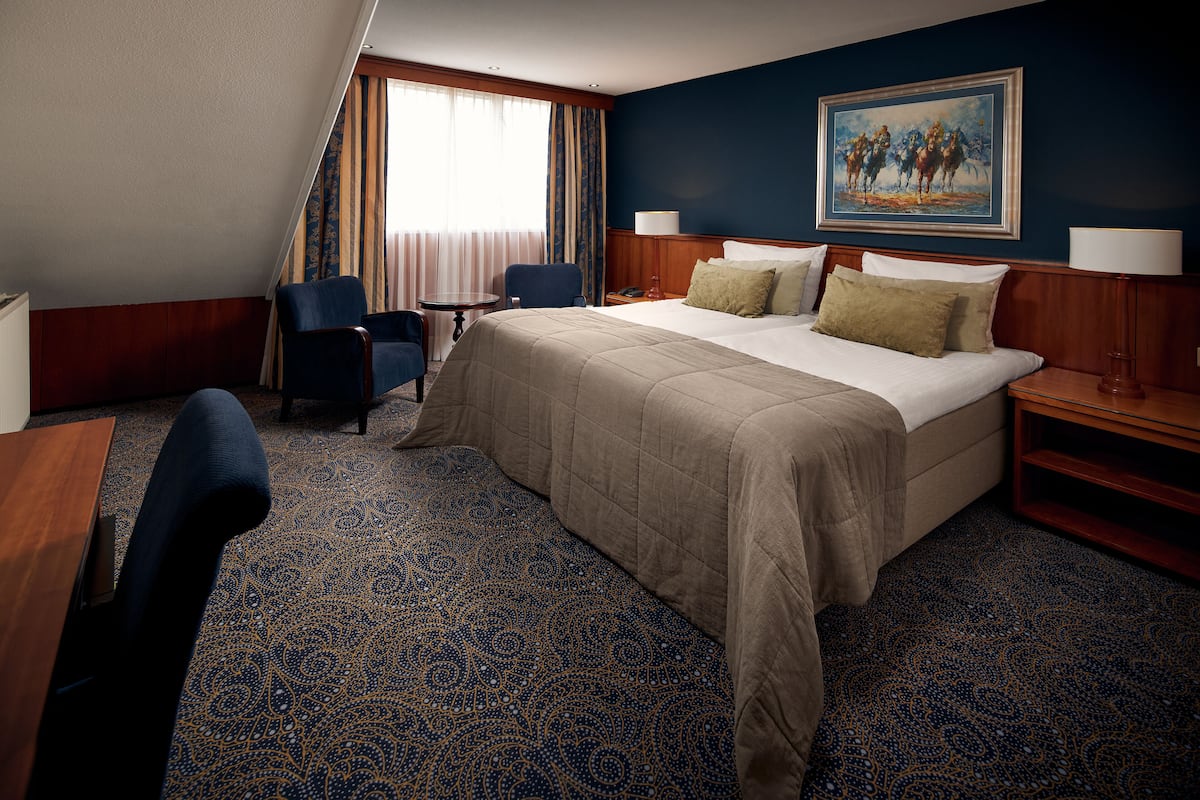 Une chambre d’hôtel avec un grand lit, deux chaises, un bureau et un tableau au mur.