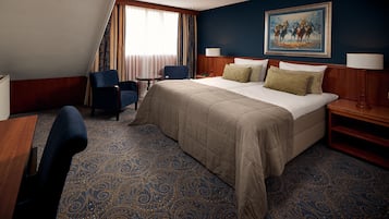 Una habitación de hotel con una cama grande, dos sillas, un escritorio y un cuadro en la pared.