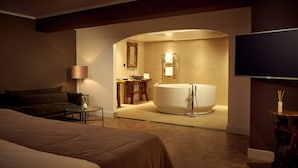 Ein modernes Hotelzimmer mit einem großen Bett, einer Sitzecke, einem Badezimmer mit Badewanne und einem Flachbildfernseher.