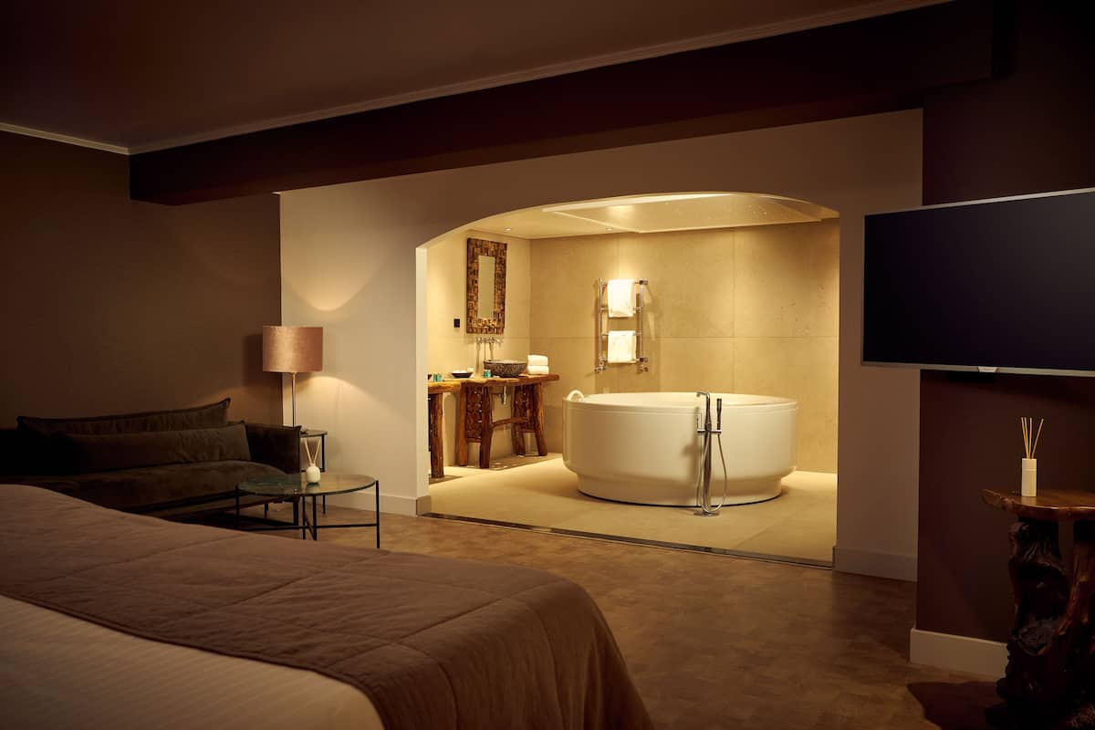 Une chambre d’hôtel moderne dotée d’un grand lit, d’un coin salon, d’une salle de bain avec baignoire et d’un téléviseur à écran plat.