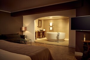 Una habitación de hotel moderna con una cama grande, una zona de estar, un baño con bañera y un televisor de pantalla plana.
