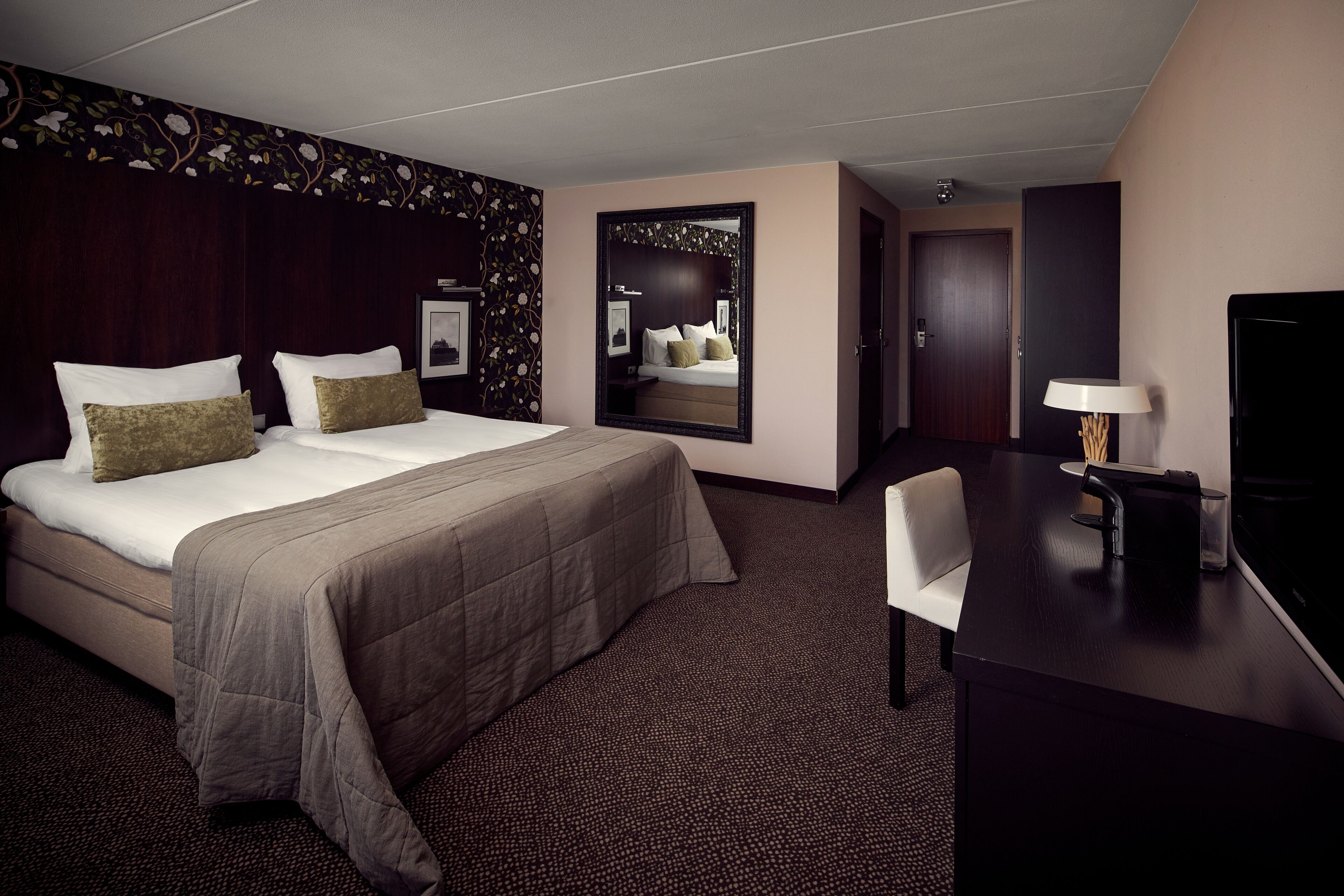 Una habitación de hotel con una cama grande, un escritorio, una silla, un televisor y un espejo.