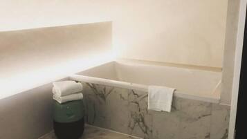 Un baño con suelo de mármol, una bañera y un cubo de basura verde.