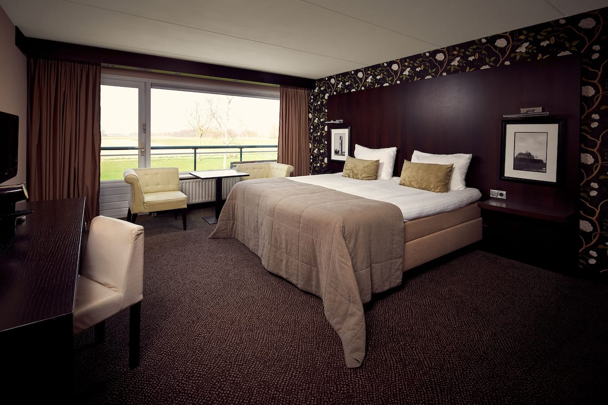 Une chambre d’hôtel avec un grand lit, un bureau, une chaise et une vue sur l’extérieur.
